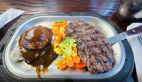 A metal plate with grilled steak, mashed potatoes with gravy, and a colorful mix of steamed vegetables.