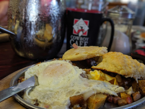 A plate of breakfast with a fried egg, biscuits, and potatoes, alongside a coffee mug from Convoy Café.
