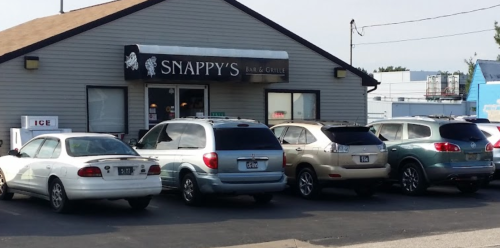 A row of parked cars in front of Snappy's Bar & Grille, a casual restaurant with a gray exterior.