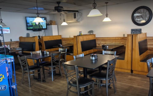 A cozy restaurant interior with wooden booths, tables, and a TV on the wall. Soft lighting creates a welcoming atmosphere.