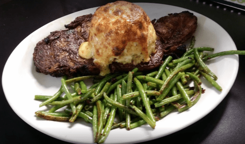 A plate featuring a grilled steak topped with a baked potato and served with sautéed green beans.