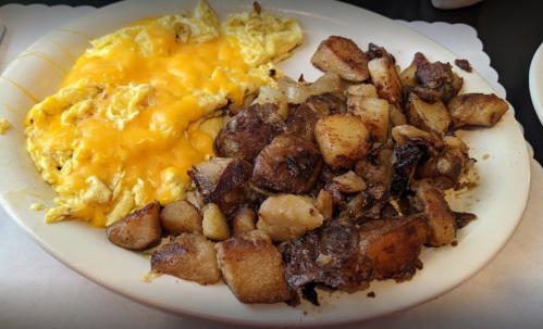 A plate featuring scrambled eggs topped with melted cheese and a side of crispy, seasoned diced potatoes.