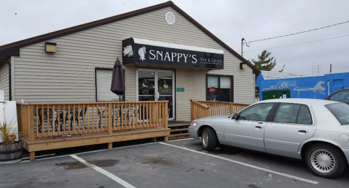 Exterior of Snappy's Bar & Grill, featuring a wooden deck and a parked car in front. Overcast sky in the background.