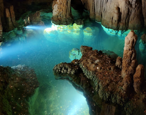 A serene underground cave with glowing blue water and illuminated rock formations.