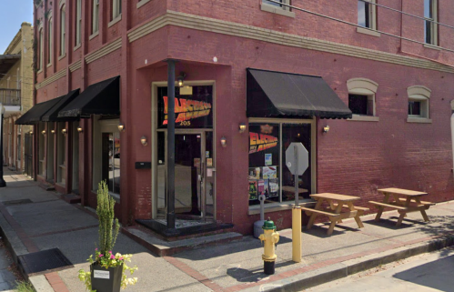 A red brick building with black awnings, featuring outdoor seating and a fire hydrant on a city street.