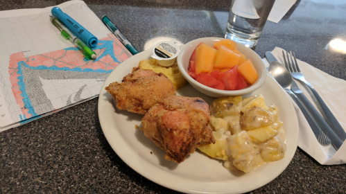 A plate of fried chicken, creamy potatoes, and fruit salad, next to a map and a glass of water on a table.