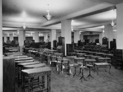A spacious furniture showroom filled with various tables and cabinets, illuminated by overhead lights.