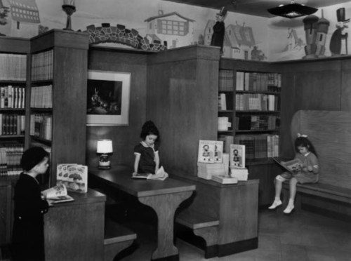 Two girls read books in a vintage library, surrounded by shelves filled with books and a cozy reading nook.