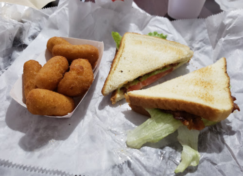 A sandwich with lettuce and tomato, alongside a small container of golden, breaded cheese bites on a paper tray.