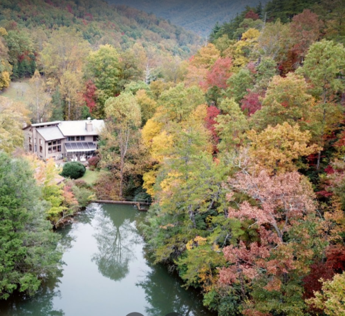 A serene cabin surrounded by vibrant autumn foliage and a calm lake in a mountainous landscape.
