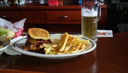 A plate with a burger, fries, and a glass of beer on a wooden table in a casual dining setting.