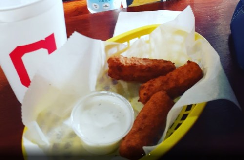 A yellow basket with three fried snacks and a small cup of dipping sauce on a wooden table.