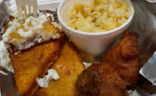 A plate of fried fish with tartar sauce, alongside a cup of macaroni and cheese.