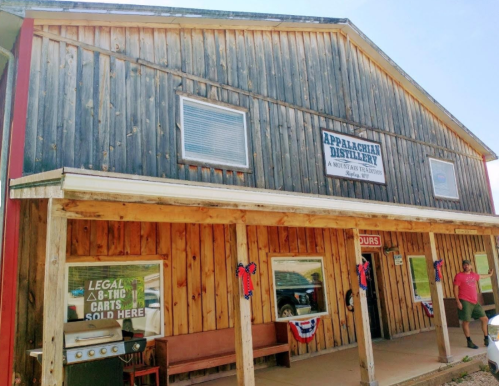 A rustic wooden distillery building with a porch, featuring patriotic decorations and a sign for Appalachian Distillery.
