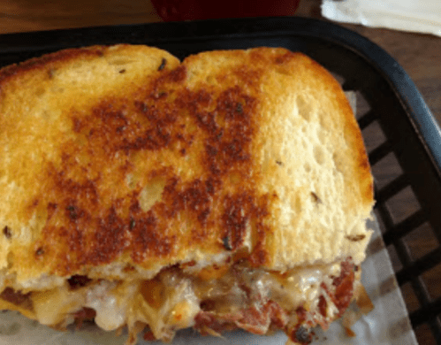 A toasted sandwich with melted cheese and a golden-brown crust, served on a black tray.