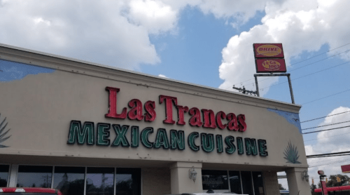 Sign for "Las Trancas Mexican Cuisine" on a restaurant building under a partly cloudy sky.