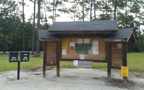 Information kiosk in a wooded area, featuring maps and park details, with a signpost nearby.