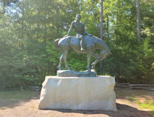 A bronze statue of a man on horseback, set on a stone pedestal, surrounded by trees.