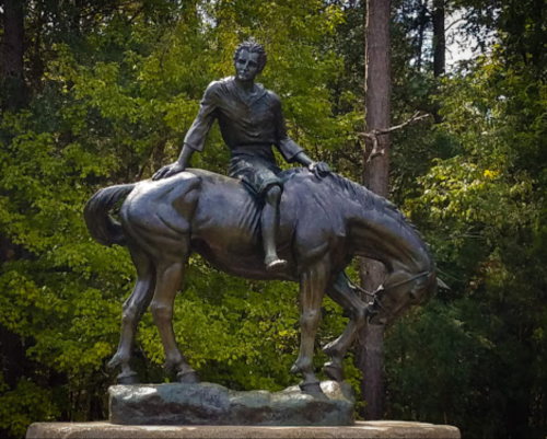 A bronze statue of a person sitting on a horse, surrounded by lush green trees.