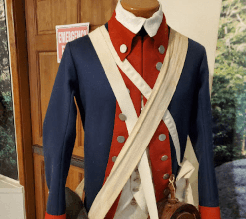 A historical military uniform featuring a blue and red coat with buttons and a shoulder strap, displayed on a mannequin.