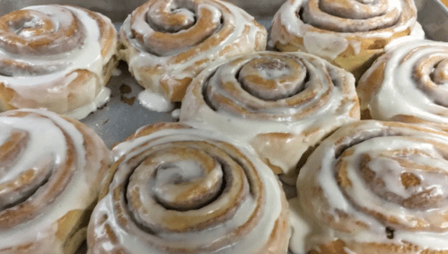 Freshly baked cinnamon rolls drizzled with creamy icing, arranged on a baking tray.