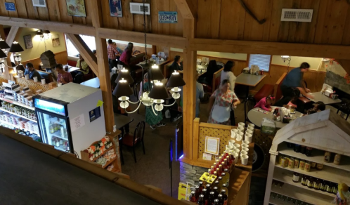 A cozy restaurant interior with diners at tables, shelves of products, and a bustling atmosphere.