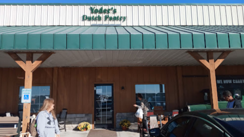 Exterior of Yoder's Dutch Pantry, featuring a green roof and wooden pillars, with people outside and a sign above the entrance.