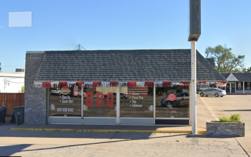 A small BBQ restaurant with a sloped roof, large windows, and festive decorations on the exterior.