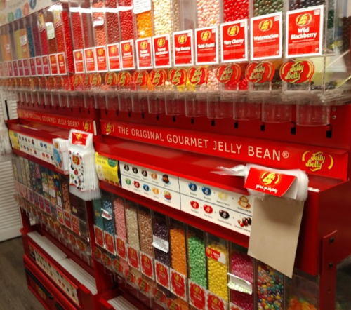 A colorful display of Jelly Belly jelly beans in various flavors, arranged in clear containers on a red vending machine.