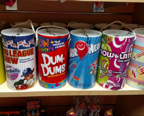 Colorful candy containers on a shelf, featuring Big League Chew, Dum-Dums, Air Heads, and Now & Later.
