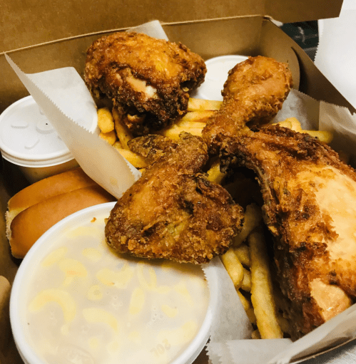 A takeout box filled with fried chicken, French fries, macaroni and cheese, and two hot dog buns.