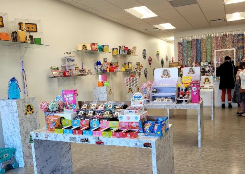 A colorful store interior filled with candy displays and various novelty items on marble tables and shelves.