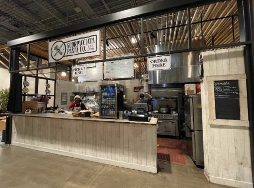 A pasta shop with a counter, menu boards, and a chef working in an open kitchen setting.