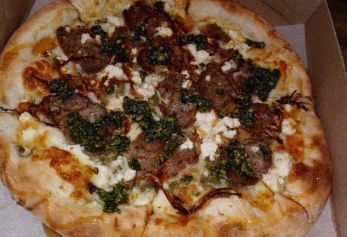 A freshly baked pizza topped with sausage, pesto, and crumbled cheese on a golden crust.
