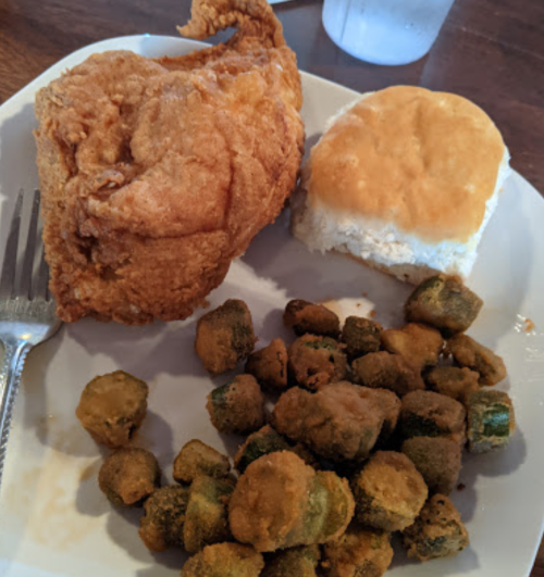 A plate with a piece of fried chicken, a biscuit, and a serving of fried okra.