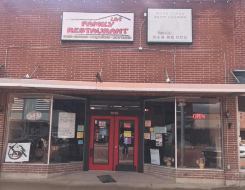 A brick building with a red door and signs for a family restaurant and barbecue, featuring an "Open" sign.