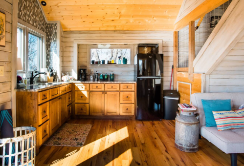 Cozy kitchen with wooden cabinets, a black fridge, and a comfortable seating area, featuring natural light and warm tones.