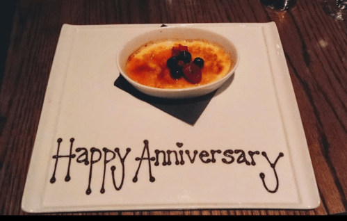 A dessert plate with crème brûlée and "Happy Anniversary" written in chocolate sauce.
