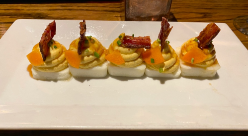 A plate of four creamy potato mounds topped with crispy bacon and orange garnish, served on a white rectangular dish.