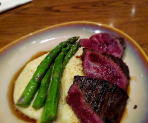 A plate featuring sliced steak, creamy mashed potatoes, and three asparagus spears, garnished with sauce.