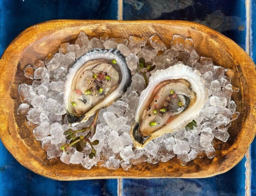 Two fresh oysters on a wooden platter, served on ice with garnishes.