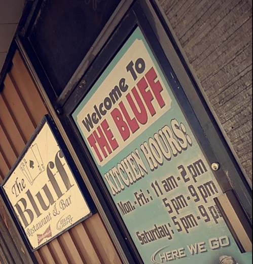 Sign for "The Bluff" restaurant and bar, displaying kitchen hours for Monday to Saturday.