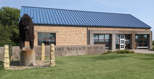 Exterior of Fort Wallace Museum featuring a bison statue and a stone building with a blue roof. Green lawn in front.