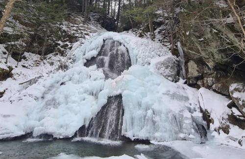 A frozen waterfall surrounded by snow-covered rocks and trees, creating a serene winter landscape.