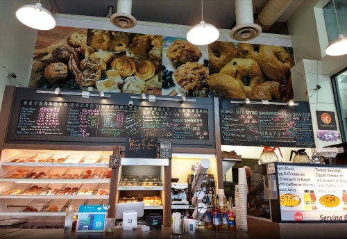 A cozy café interior featuring a menu board, baked goods display, and a wall mural of various pastries.