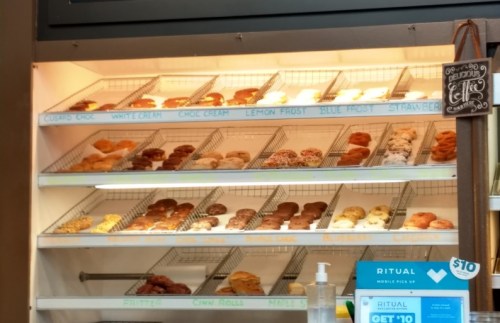 A display case filled with various donuts, including glazed, frosted, and filled options, labeled with flavors.