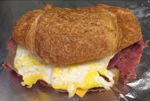 A croissant sandwich filled with eggs and slices of roast beef, resting on a silver foil surface.
