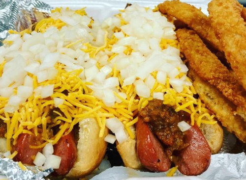 Two loaded hot dogs topped with cheese and onions, served with crispy fried strips on the side.