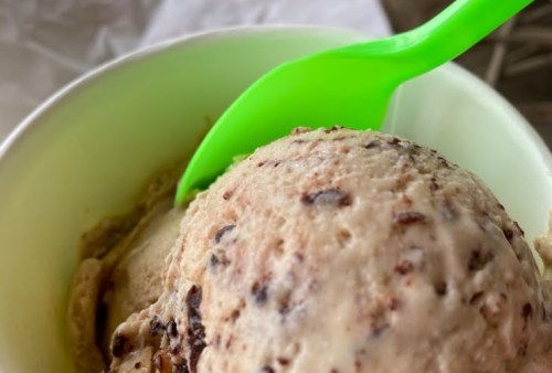 A close-up of a scoop of ice cream in a cup, with a bright green spoon resting on top.