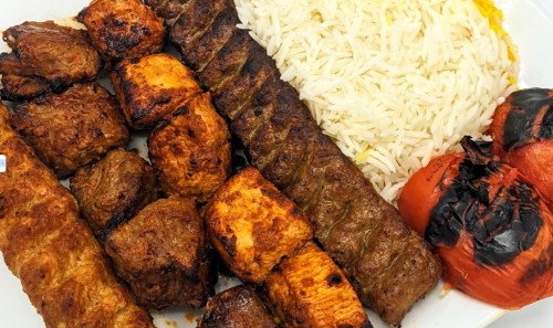 A platter of grilled kebabs, including beef and chicken, served with fluffy rice and charred tomatoes.